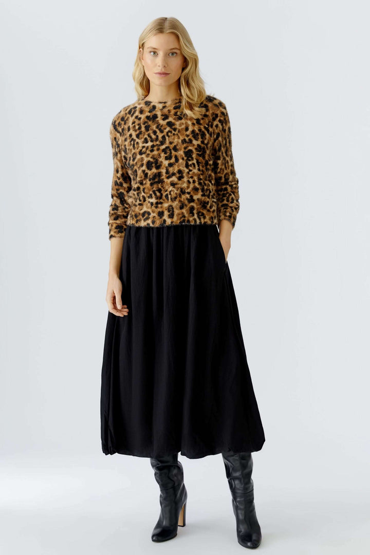 Femme portant un chandail duveteux à motif animal avec une jupe longue noire et des bottes.