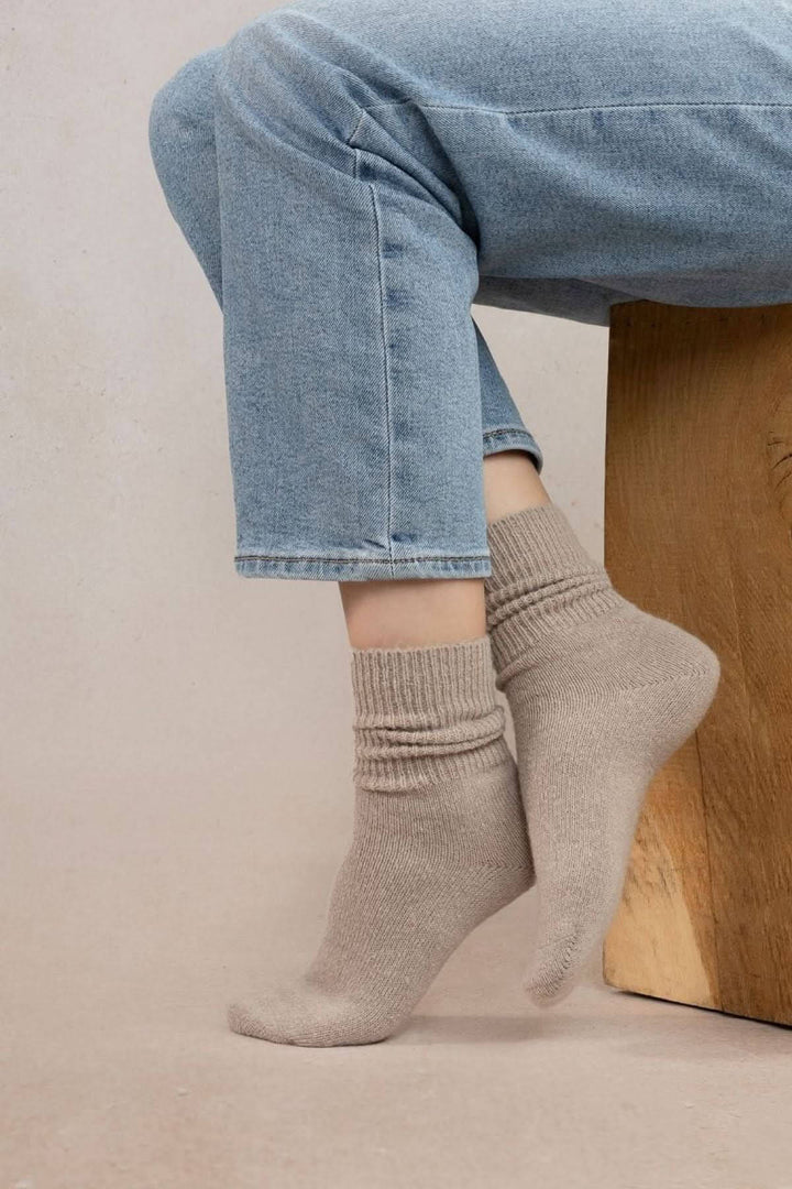 Chaussettes en laine alpaga, douces et chaudes, portées avec un jean sur un tabouret en bois.