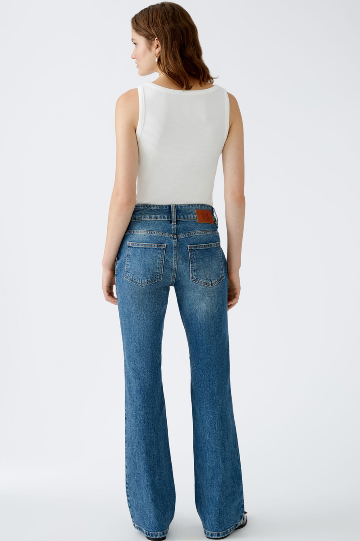 Femme de dos portant un jean taille mi-haute évasé, denim élastique, avec deux poches à l'arrière.