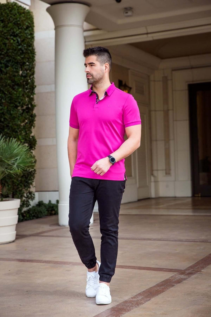 Homme portant un polo rose moderne avec col structuré et pantalon noir, déambulant dans un cadre élégant.