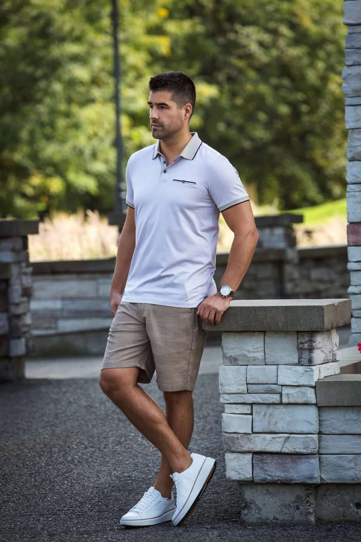 Homme portant un polo Mayberry élégant avec détails contrastants, shorts beiges et baskets blanches, en extérieur.