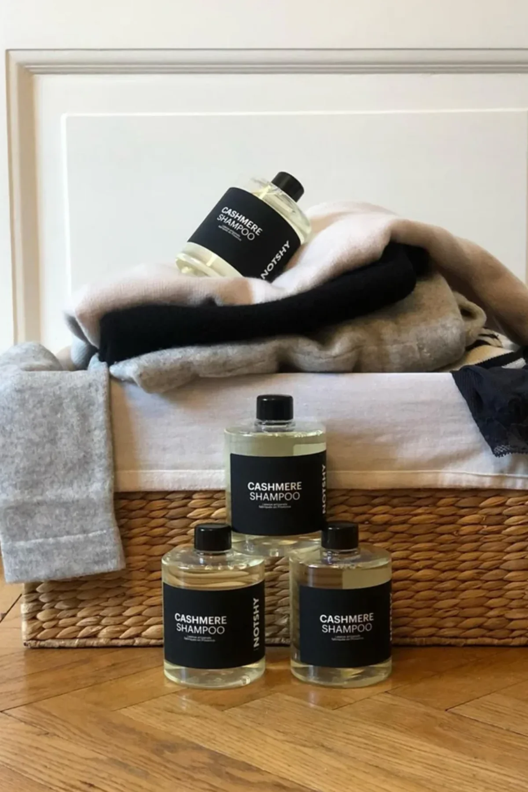 Bouteilles de shampooing cashmere avec des vêtements en cachemire dans un panier en osier sur un sol en bois.