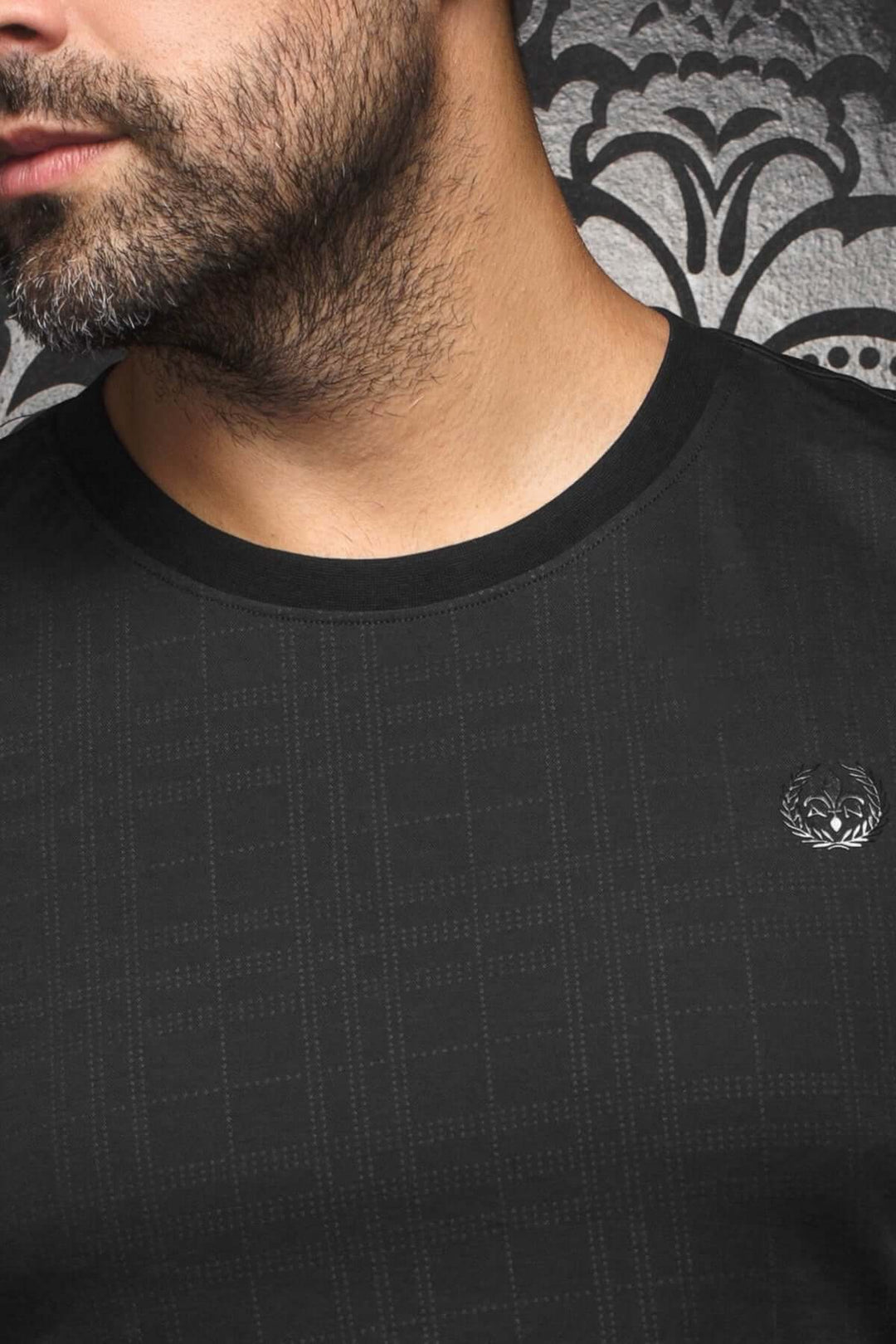 T-shirt Varenna moderne col rond noir avec motif texturé et logo brodé sur fond décoratif.