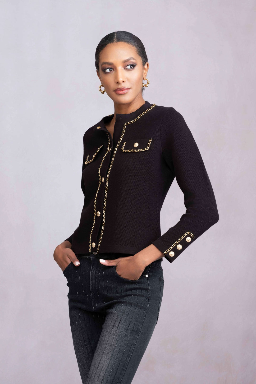 Veste de tricot boutonnée noire avec détails en chaînettes et boutons bijou, portée avec un style chic.