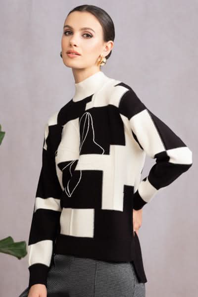 Tricot col montant noir et blanc avec fleur brodée et patchs texturés, coupe régulière et longue à l'arrière.