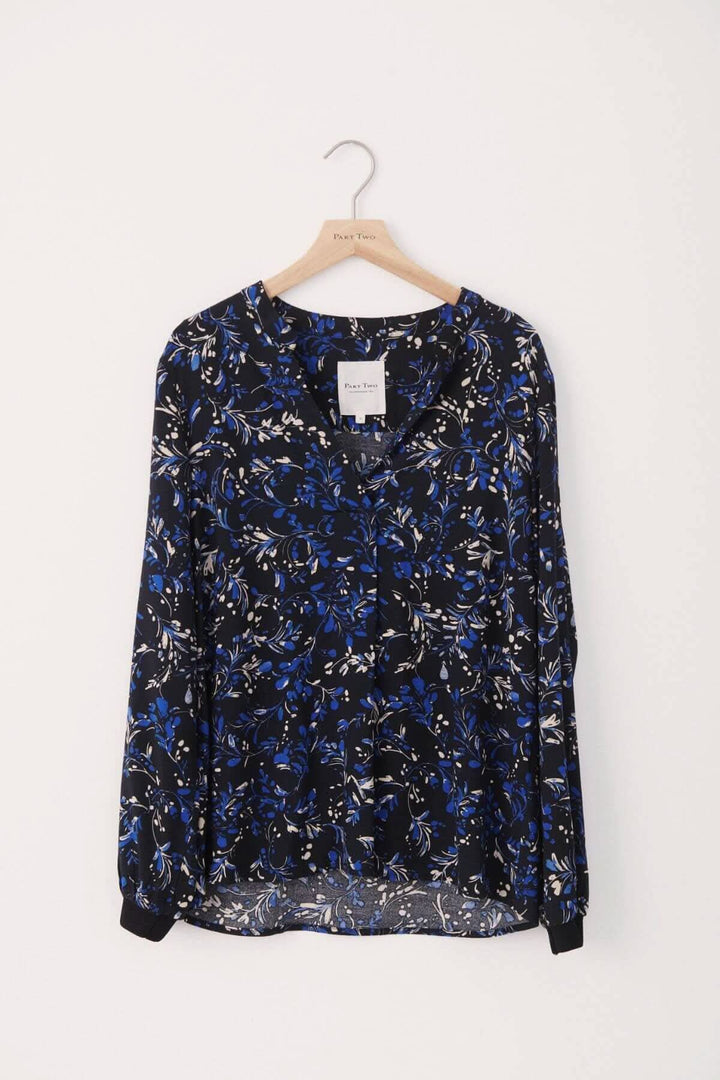 Blouse Tonnie imprimé à fleurs bleues sur fond marine, col mao, manches longues, style décontracté et confortable.