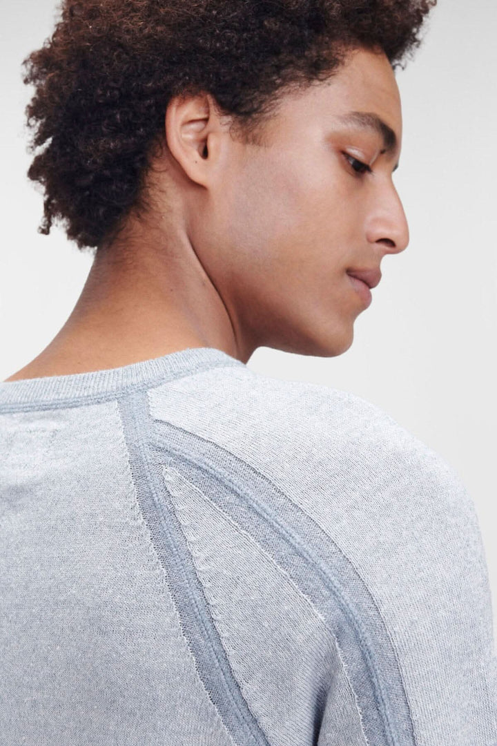 Homme portant un pull en coton gris, montrant le col ras du cou et les coutures distinctives aux épaules.