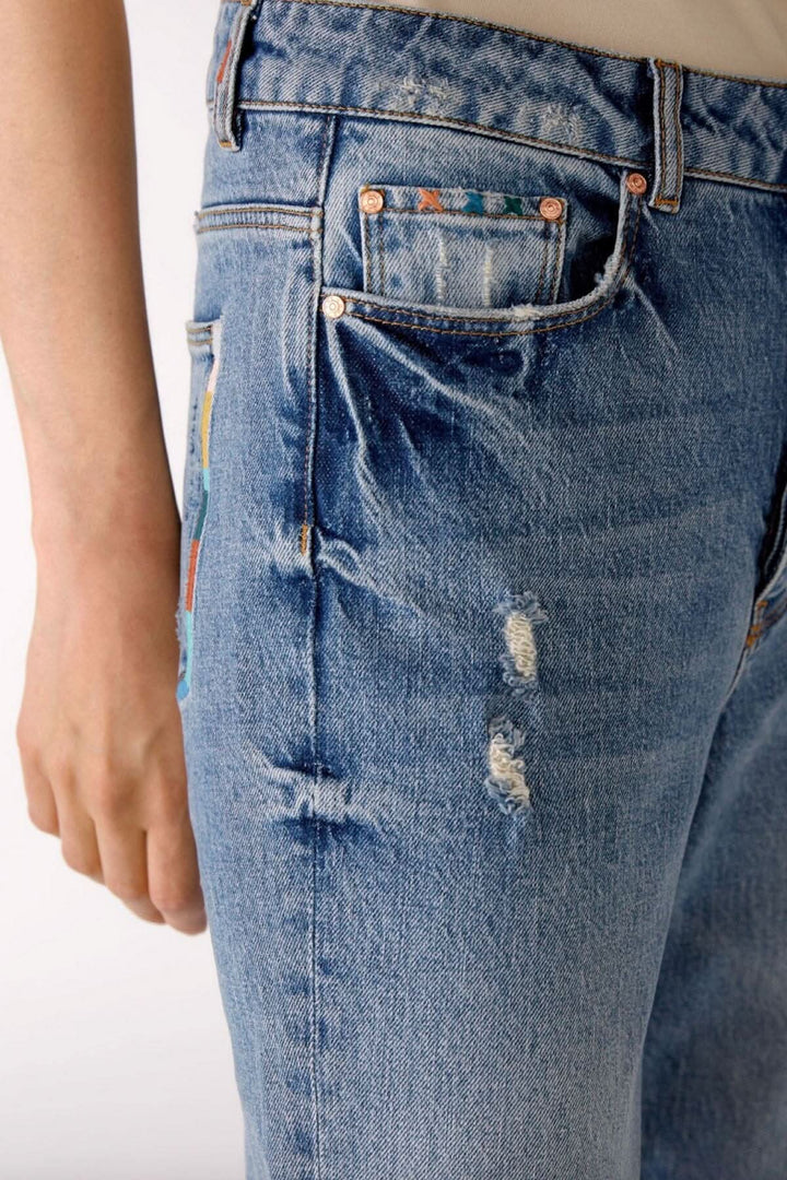 Jean pâle à jambe droite avec détails de coutures colorés et décolorations, style décontracté.