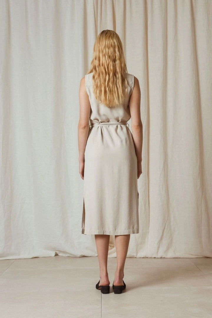 Femme vue de dos portant une robe en piqué de lyocell, avec ceinture et ouvertures latérales, sur fond neutre.