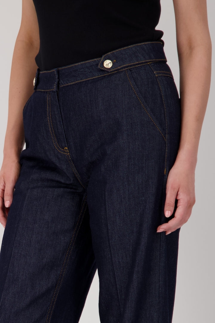 Jean taille haute en denim brut, coupe droite avec ceinture à passants et boutons métalliques.