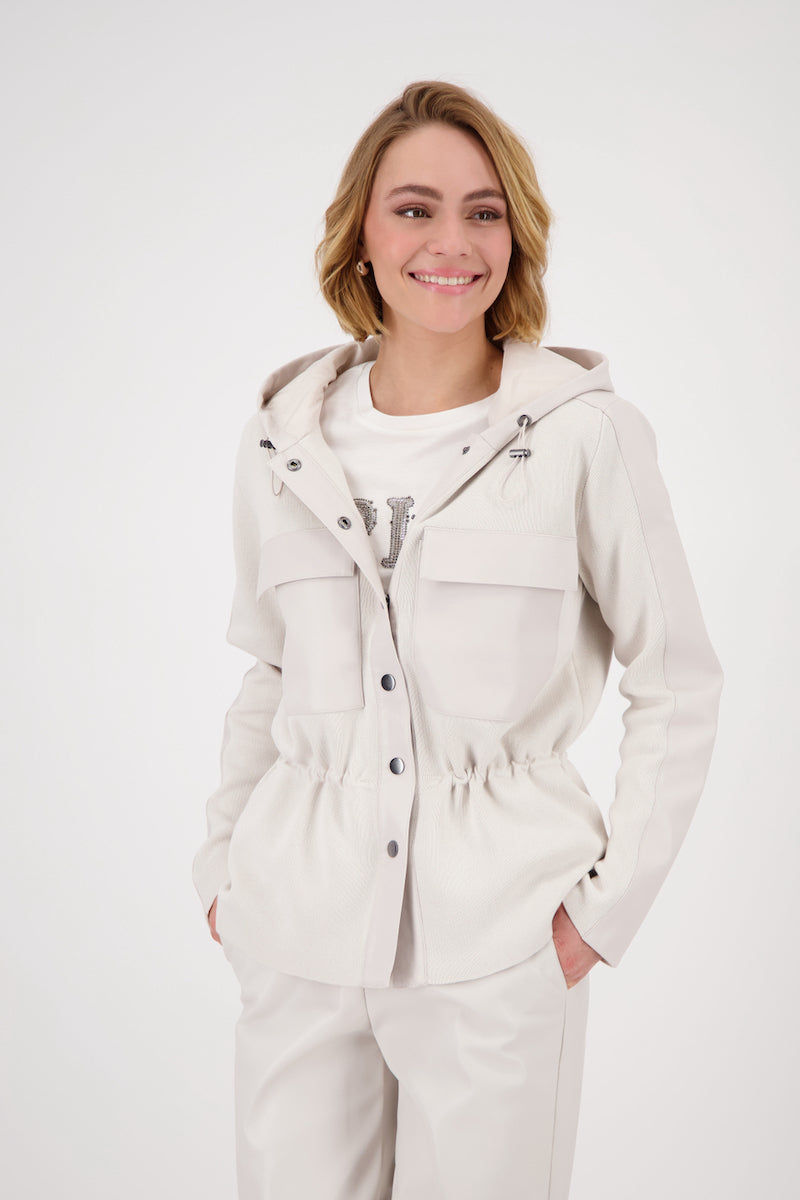 Femme souriante portant une veste à capuchon beige avec cordon de serrage et poches, style décontracté.