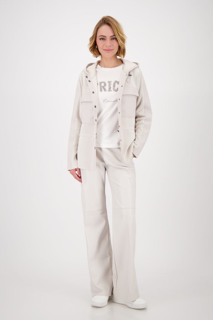Femme portant une veste à capuchon beige et un pantalon assorti, style décontracté avec un t-shirt graphique.