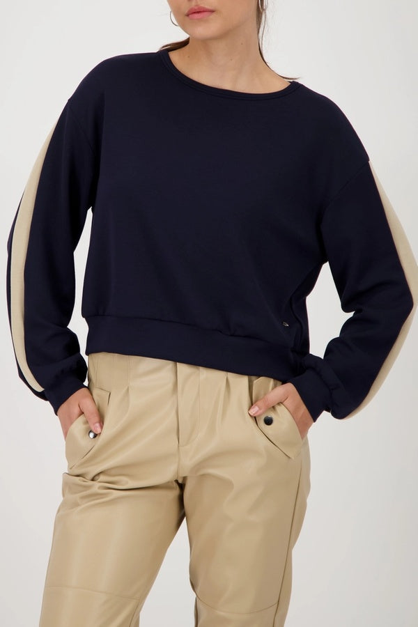 Femme portant un chandail à bandes contrastées sur les manches avec col rond et coupe droite, style sport-chic.
