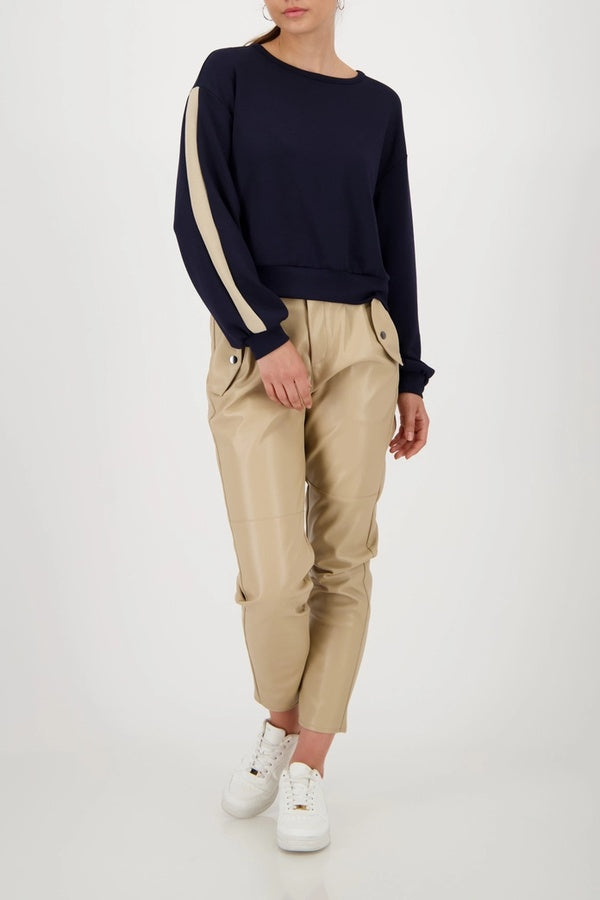 Femme portant un chandail à bandes contrastées sur les manches, col rond, coupe droite, avec pantalon en cuir beige, look sport-chic.