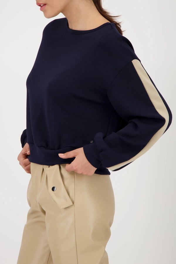 Chandail à bandes contrastées sur les manches en bleu marine avec col rond, porté avec un pantalon beige pour un look sport-chic.