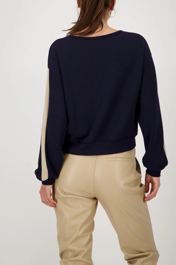 Femme portant un chandail à bandes contrastées sur les manches et un pantalon beige, vue de dos, col rond, style décontracté et chic.