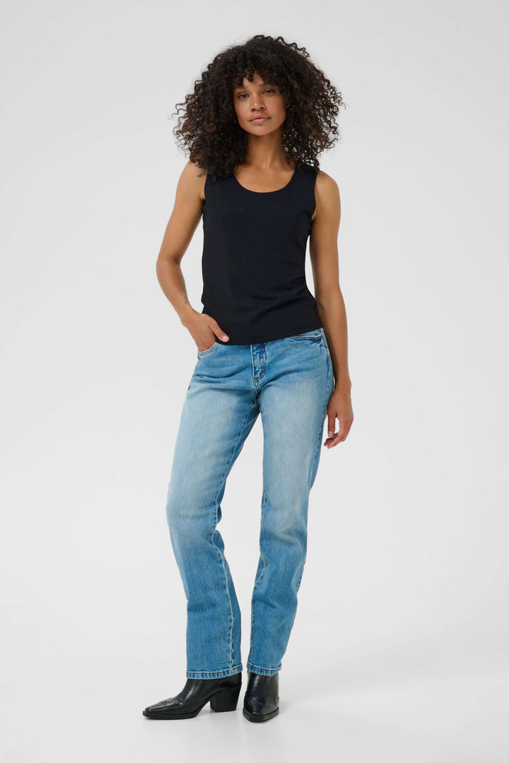 Woman wearing black tank top and blue jeans standing confidently against a light background