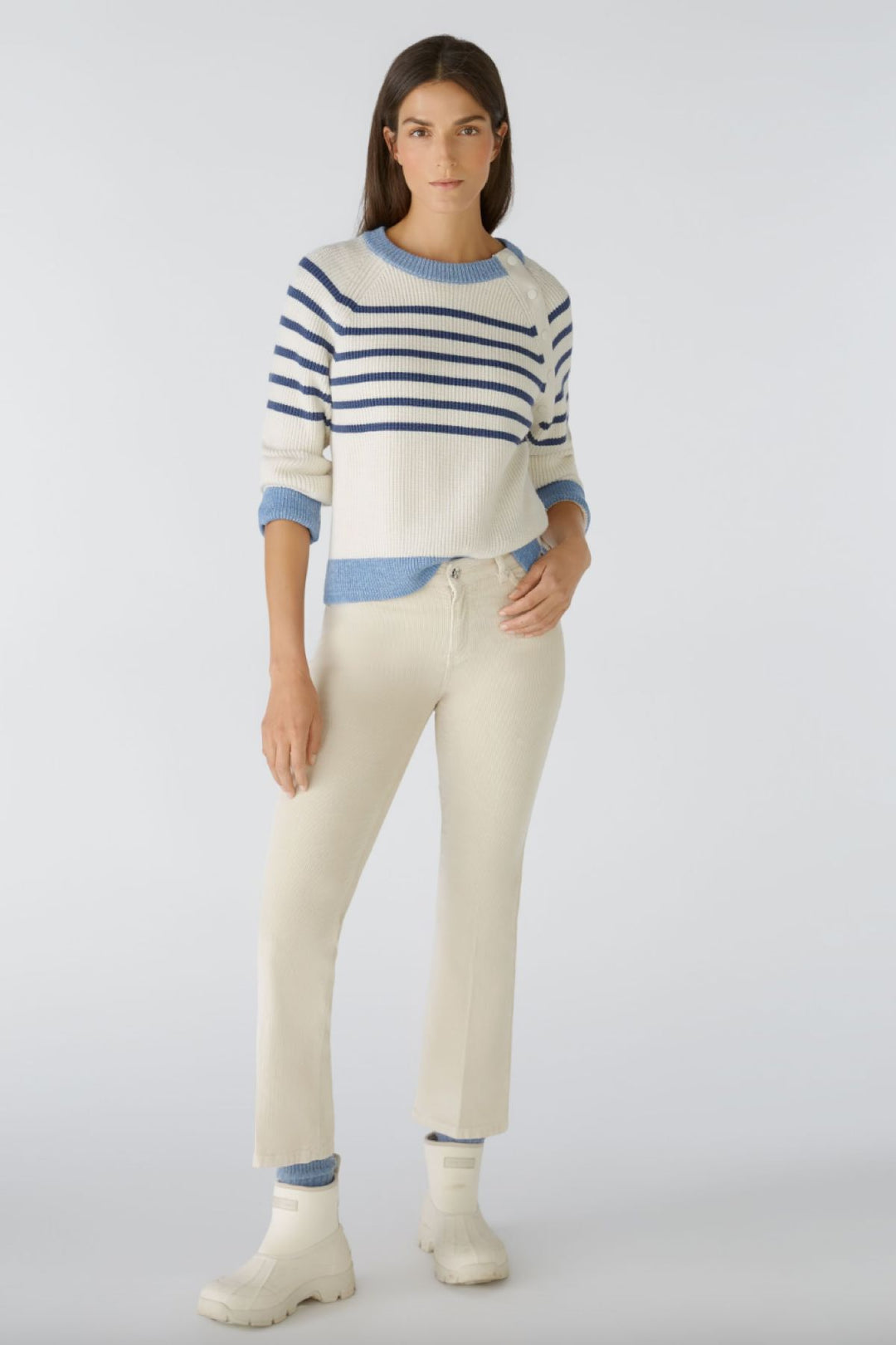 Femme portant un pulls rayé et un pantalon en velours côtelé, avec des bottes blanches, dans un style décontracté.