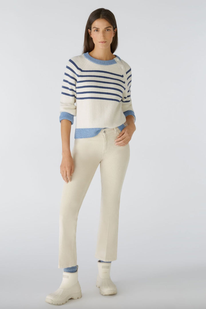 Femme portant un pulls rayé et un pantalon en velours côtelé, avec des bottes blanches, dans un style décontracté.