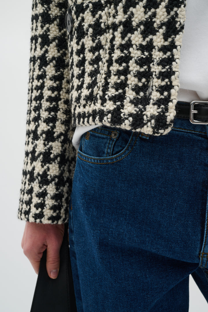Détail d'une veste courte à motif pied-de-poule portée avec un pantalon denim, alliant élégance et modernité.