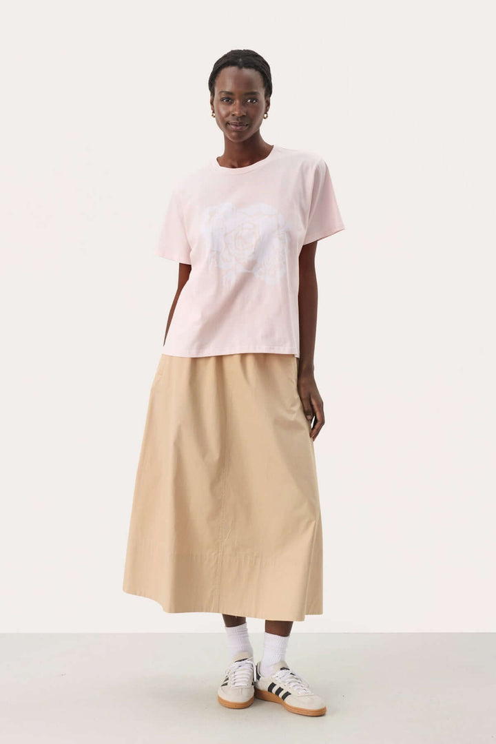 Femme portant un t-shirt en coton biologique rose avec un imprimé artistique et une jupe longue beige.