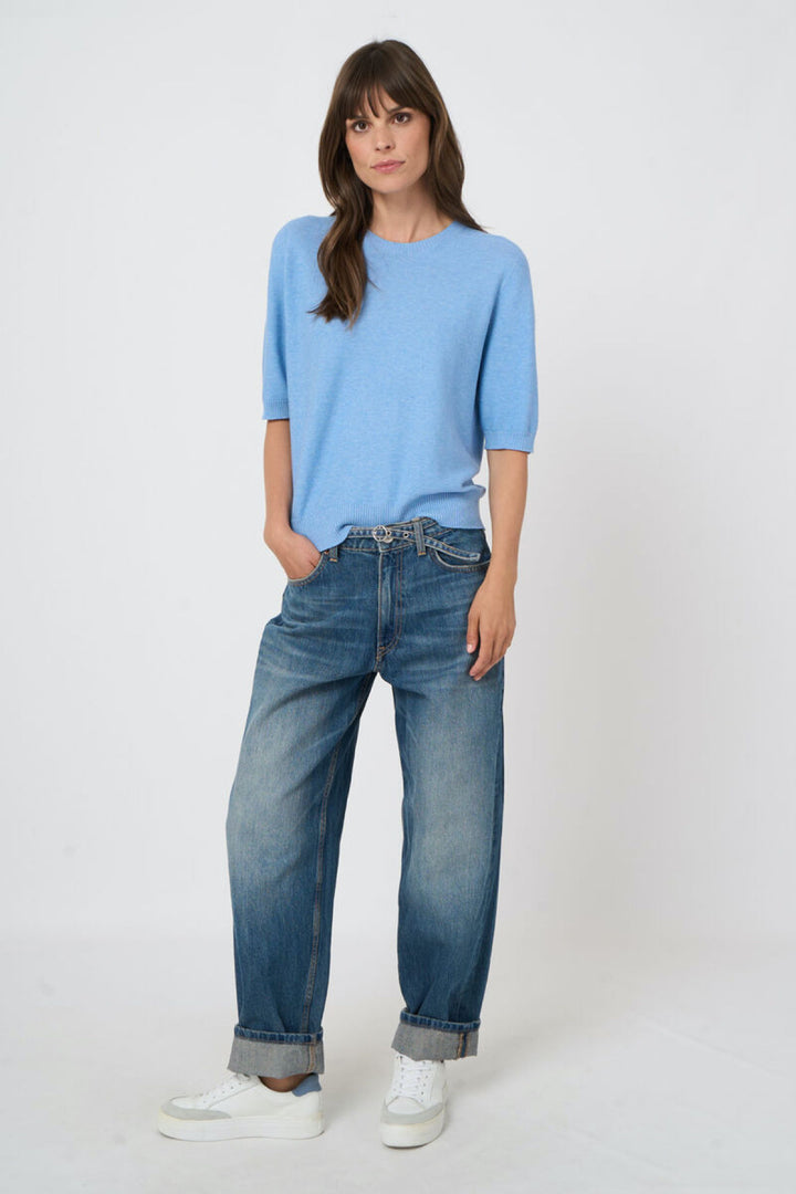 Femme portant un tricot à manches courtes bleu, style élégant et minimaliste, avec un jean ample, idéal pour la saison.