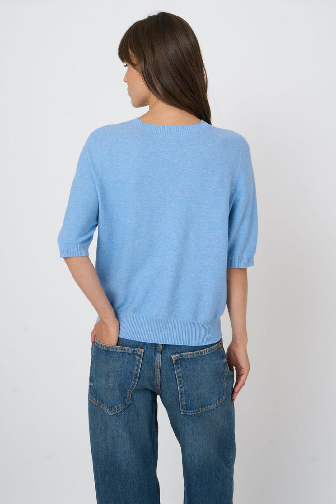 Tricot à manches courtes bleu en maille fine, silhouette élégante et minimaliste, modèle femme de dos.