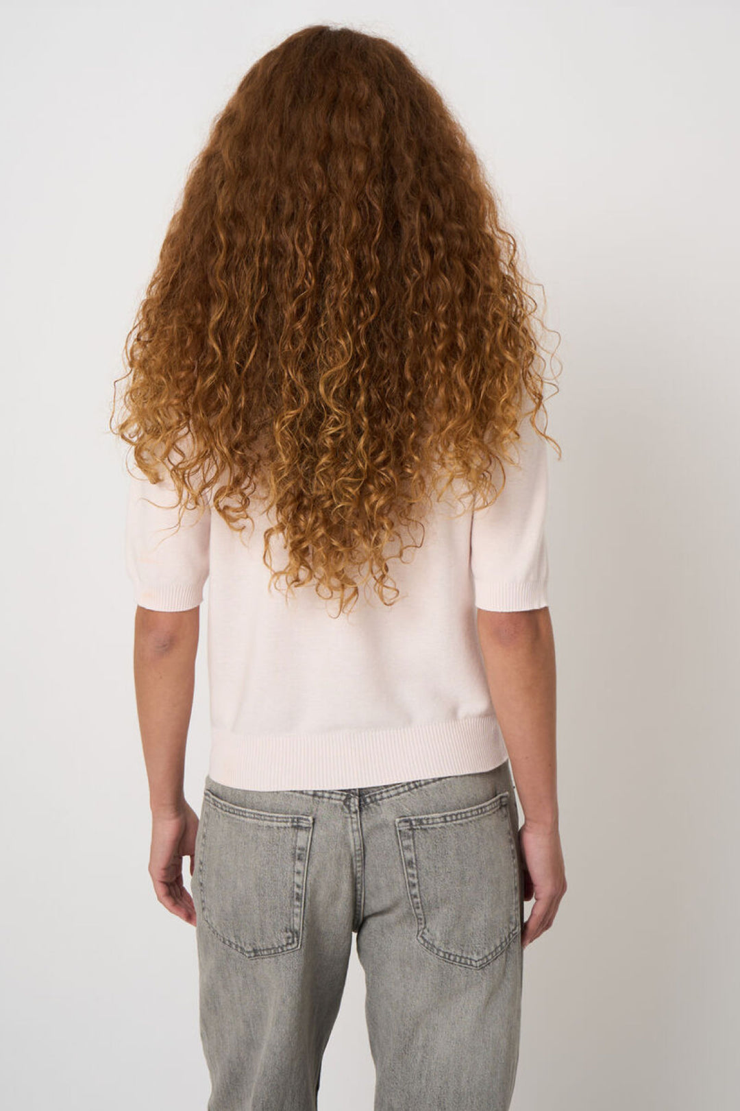 Vue arrière d'un tricot à manches courtes rose, porté avec un jean, mettant en évidence sa silhouette minimaliste et sa maille douce.