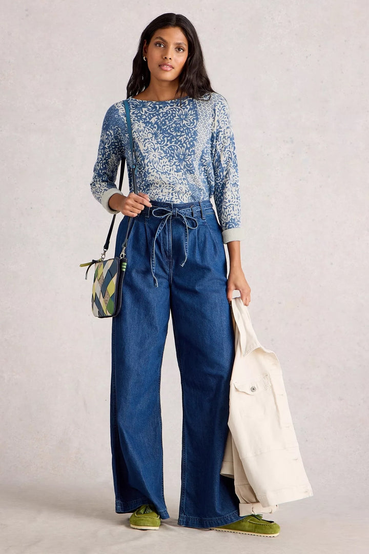 Femme portant un chandail imprimé bleu et un pantalon large, avec un sac à main moderne et un style chic.