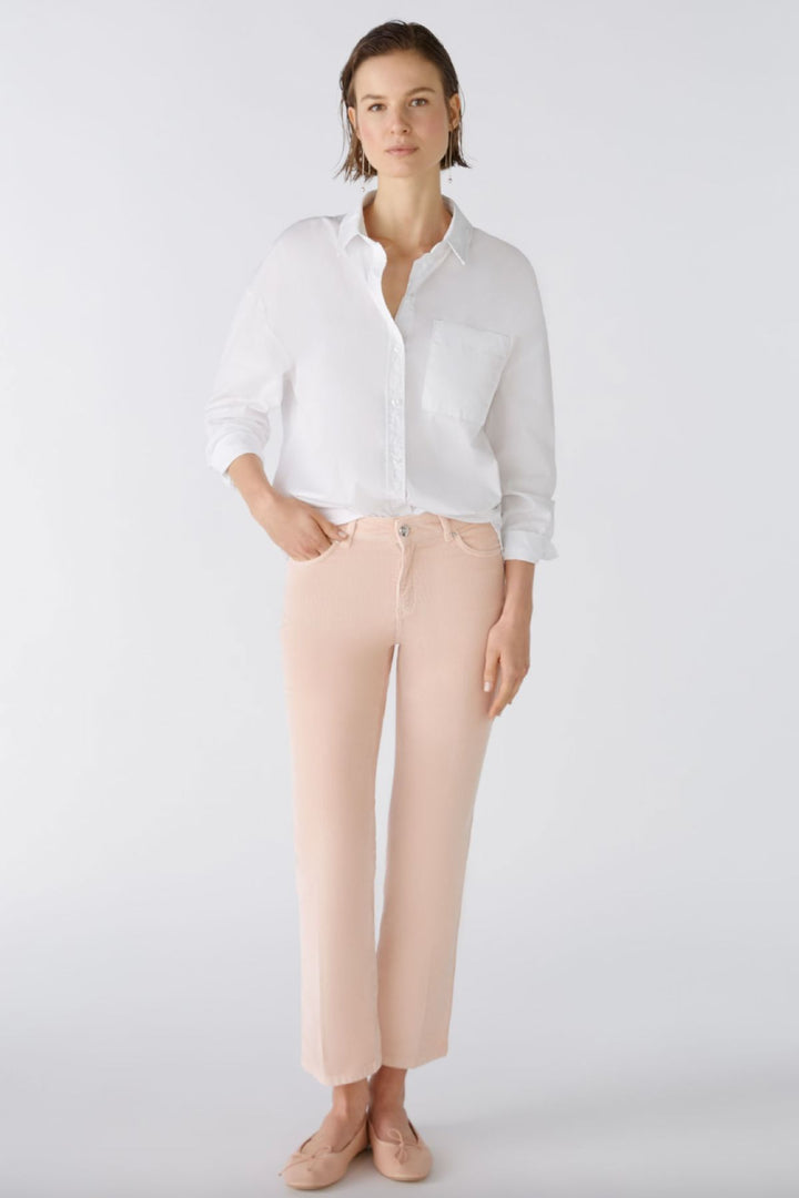 Femme portant un pantalon en velours côtelé rose et une chemise blanche, style décontracté, devant un fond blanc.