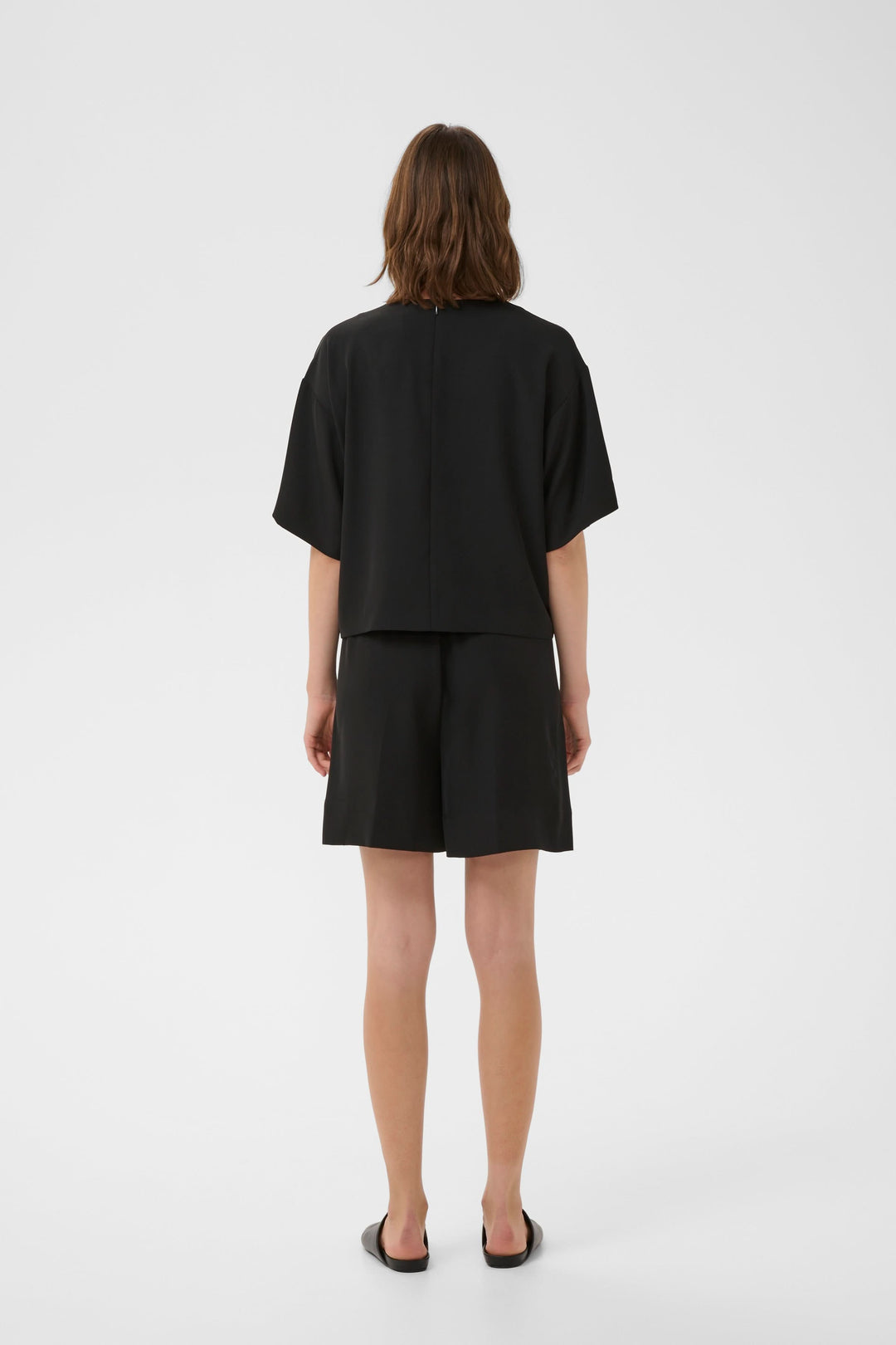 Femme portant un Bermuda Varina fluide taille élastique ceinturé avec coupe droite et poches latérales, vu de dos en studio.