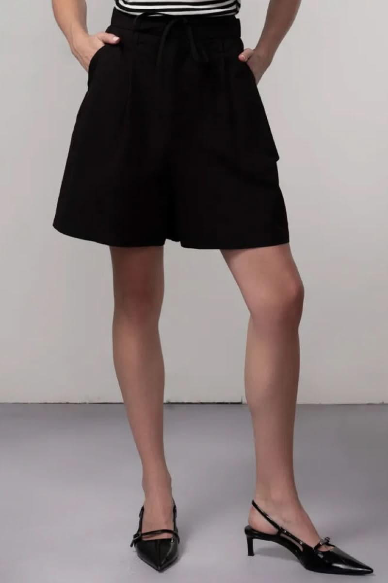 Femme portant un Bermuda coupe fluide noir, silhouette élégante et moderne pour une tenue estivale décontractée ou habillée.