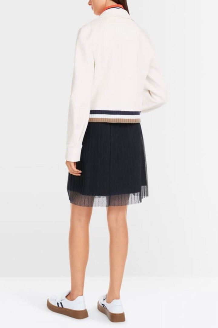 Back view of a woman in a white blazer and black pleated skirt, showcasing a stylish preppy look.