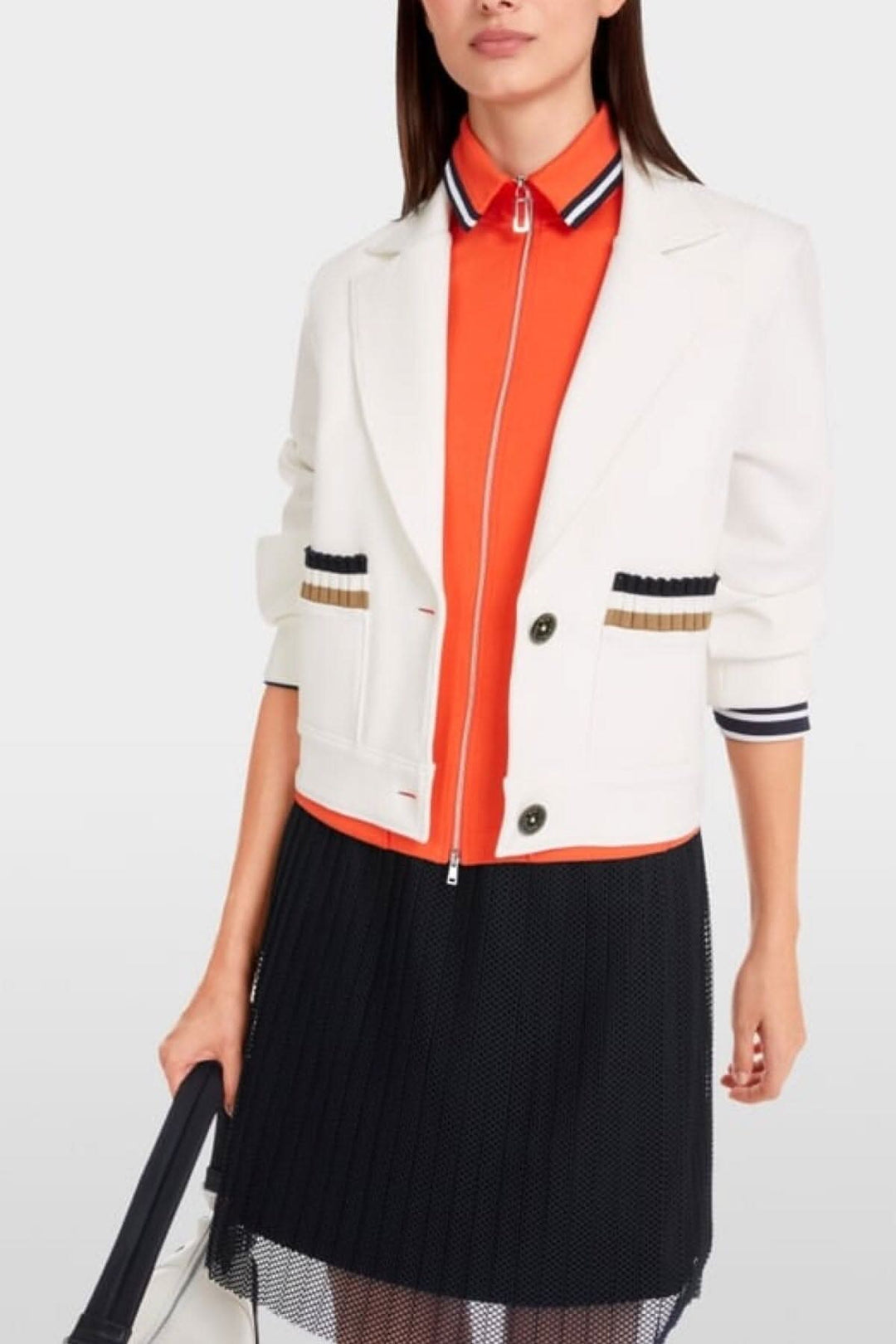 Woman wearing a stylish white jersey blazer with striped pocket details and an orange shirt, paired with a black skirt.