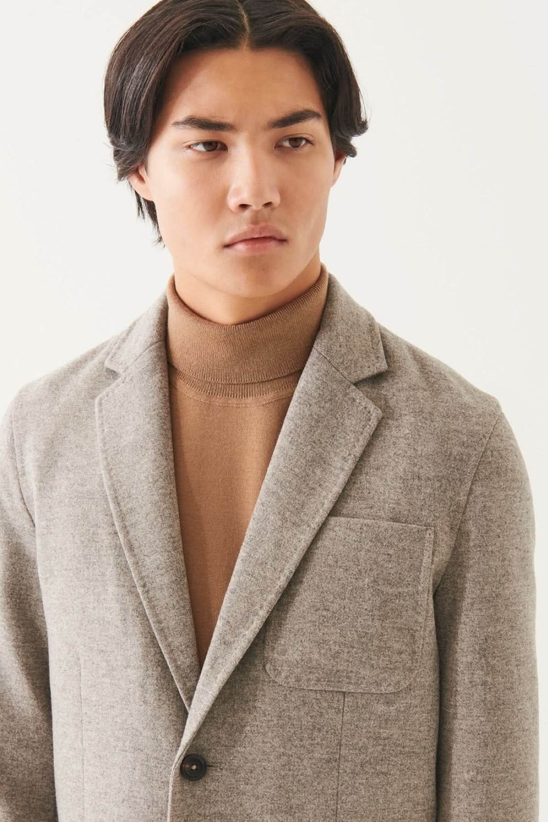 Homme portant un blazer en laine à deux boutons, avec un col roulé beige, style oversized moderne.