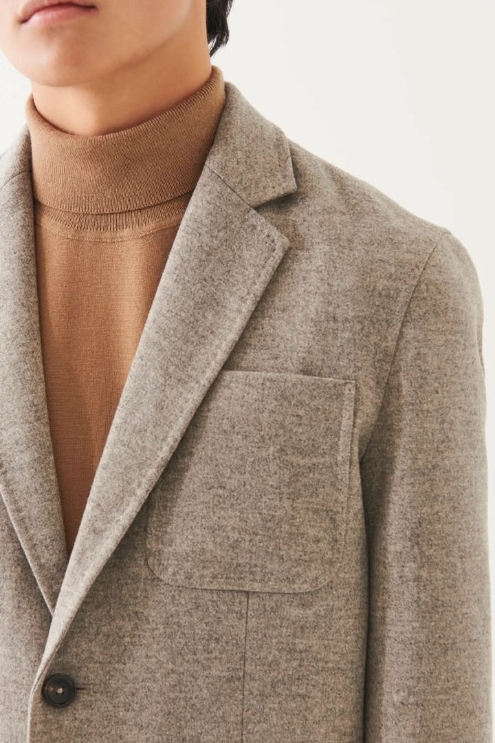 Blazer en laine à deux boutons avec col, porté sur un pull beige, mettant en avant sa texture douce et sa coupe élégante.