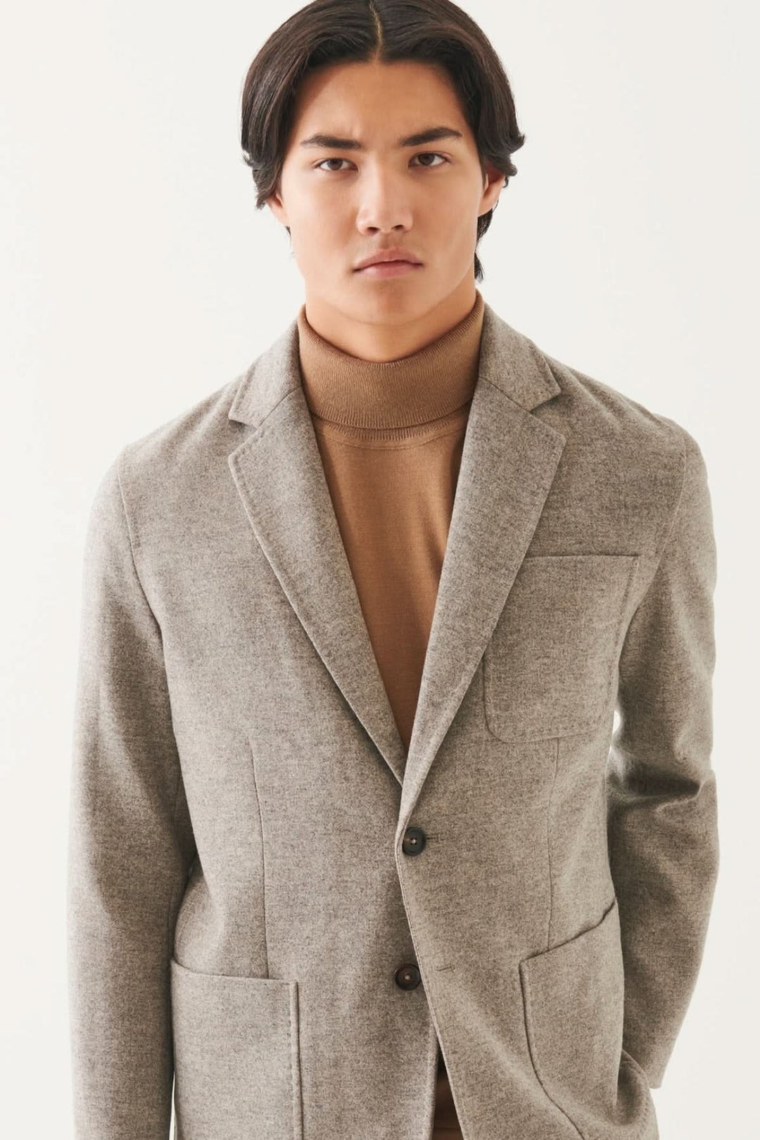 Blazer en laine à deux boutons, couleur gris, porté par un homme avec un col roulé beige.