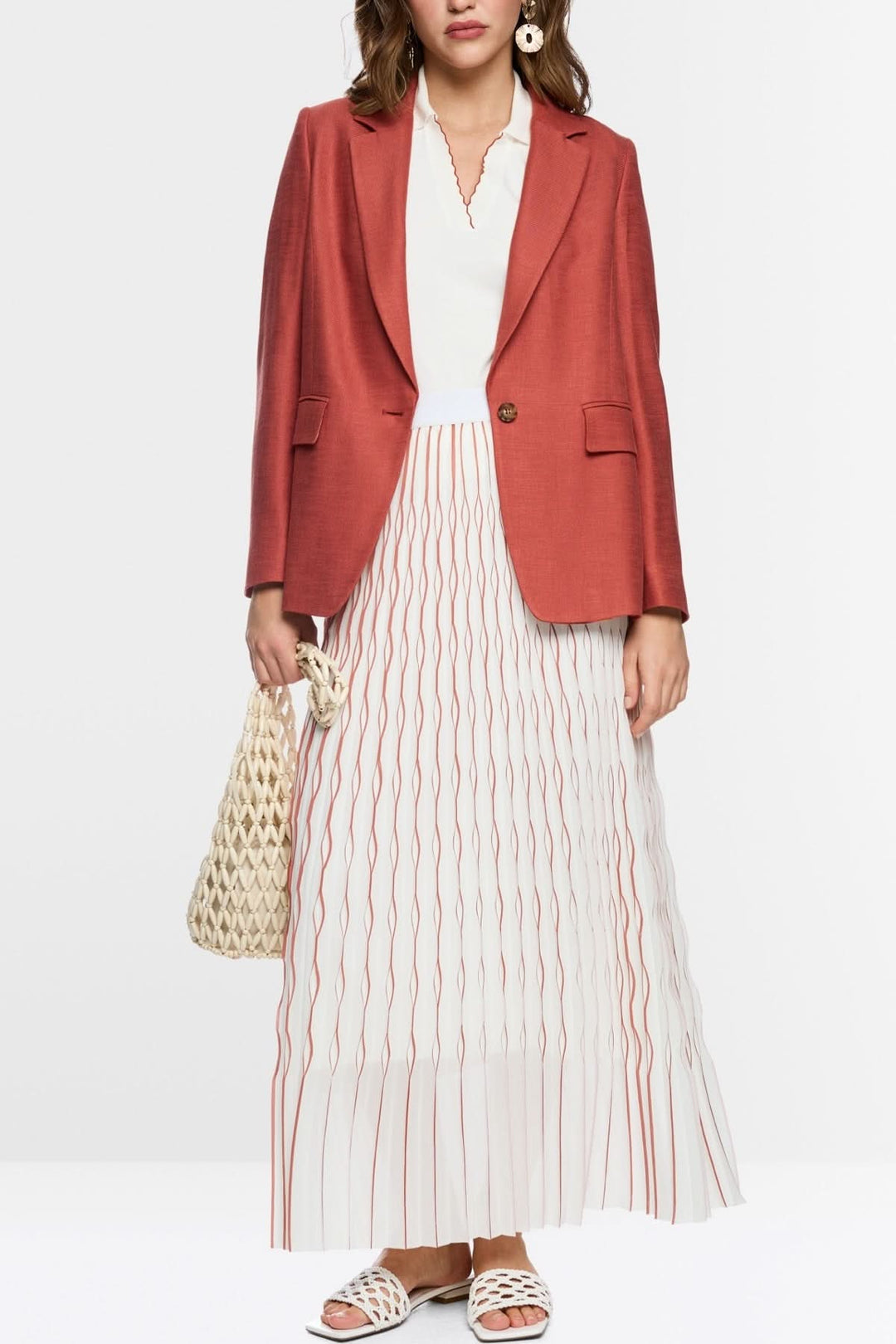Blazer structuré à bouton unique porté avec jupe plissée et haut blanc moderne, soulignant l&