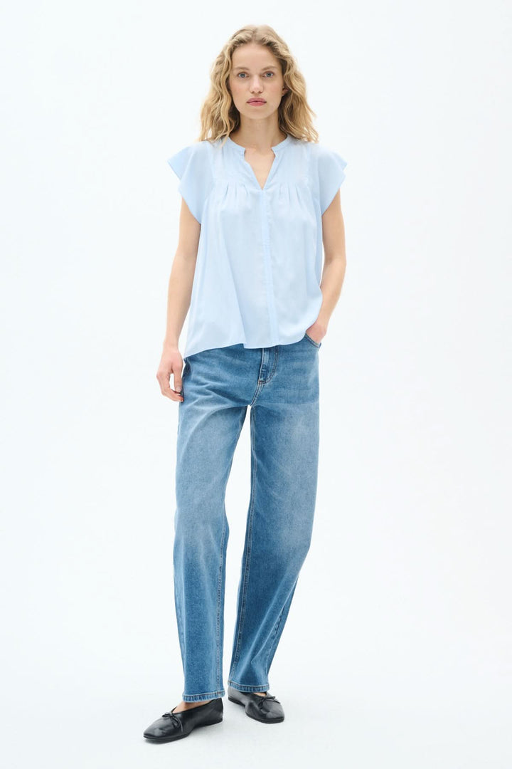 Light blue blouse with pleated neckline and flutter sleeves paired with relaxed fit jeans.