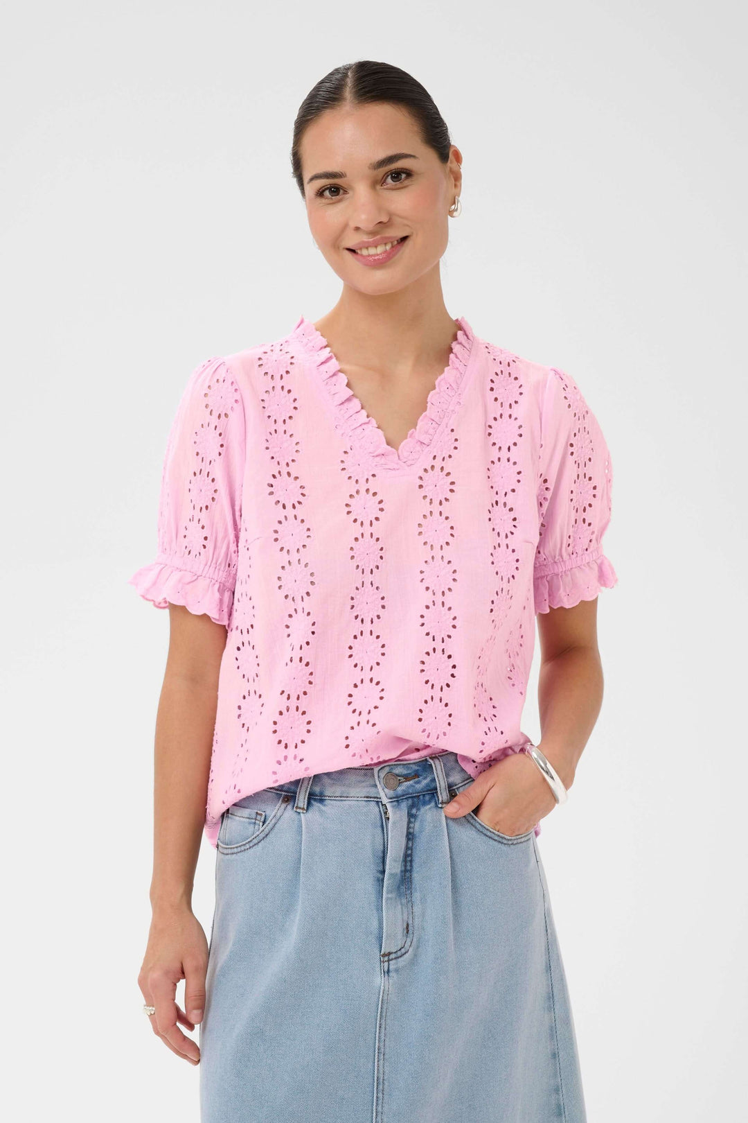 Femme portant la Blouse Dona brodée à manches courtes avec encolure volantée, détails ajourés pour un look élégant et décontracté.
