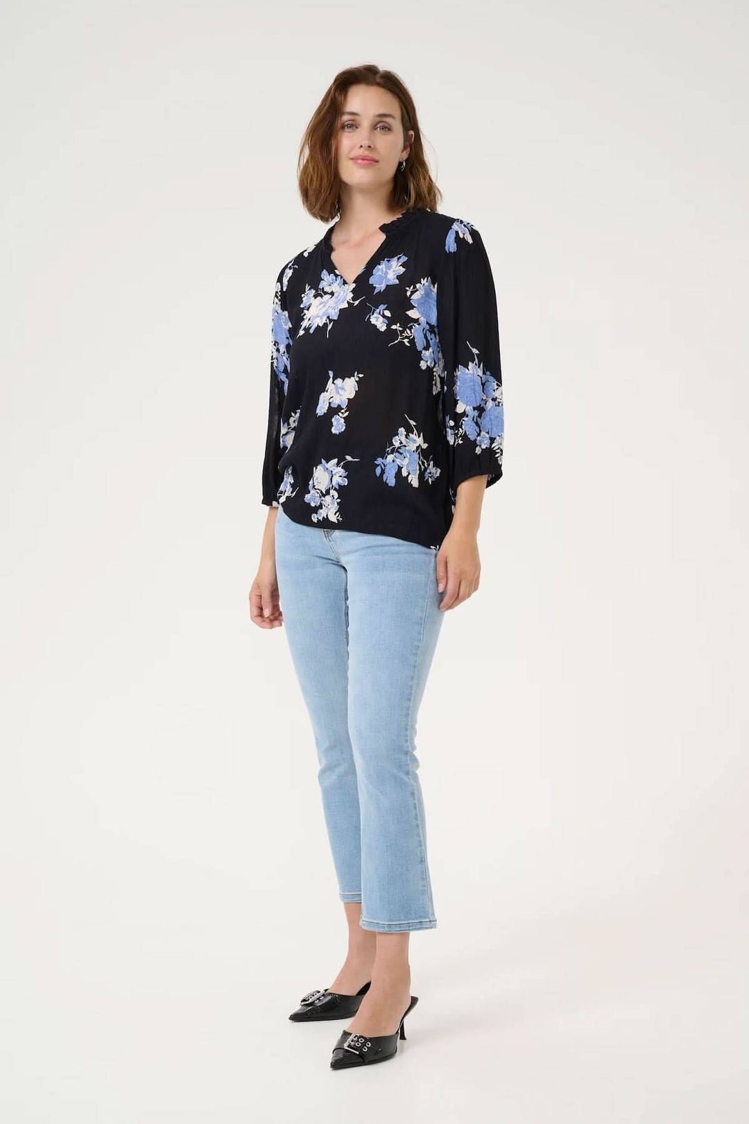 Femme portant la blouse Edita à imprimé floral, encolure froncée, manches 3/4, style décontracté avec jean.