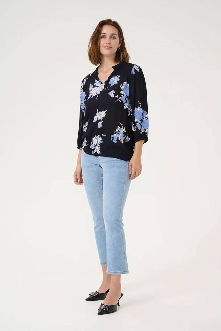 Femme portant la blouse Edita à imprimé floral, encolure froncée, manches 3/4, style décontracté avec jean.