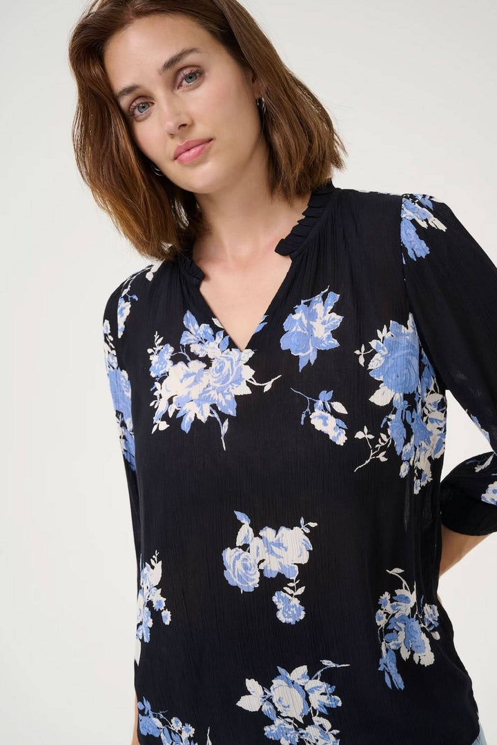 Femme portant une blouse fluide noire à imprimé floral bleu, encolure V et manches 3/4.