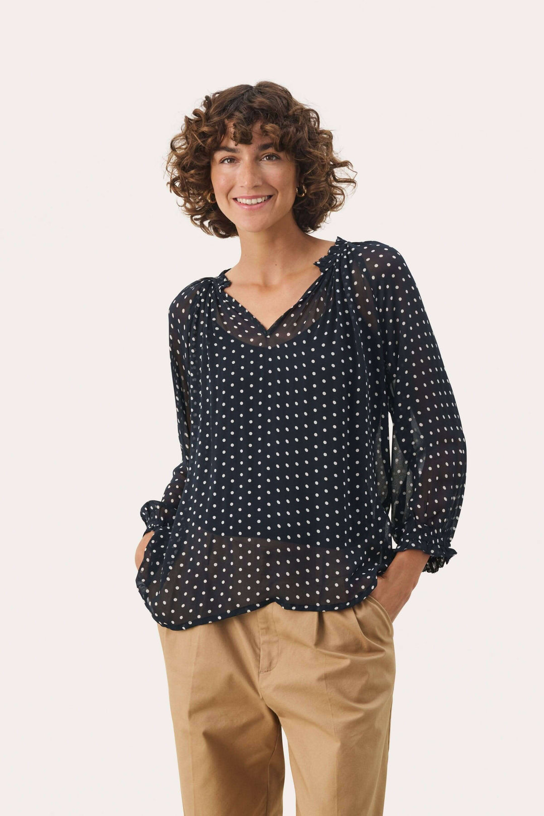 Femme portant une blouse Elsia en viscose noire à pois, avec manches 3/4 et coupe décontractée, associée à un pantalon beige.