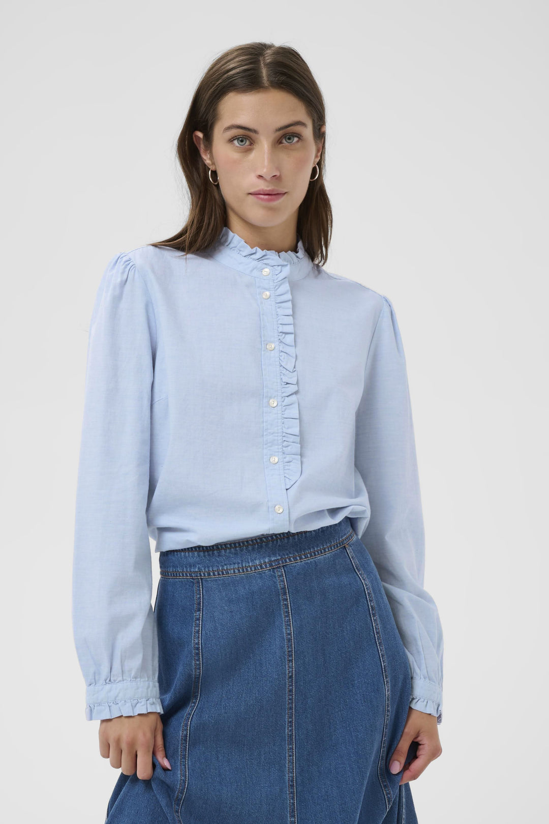 Blouse Glessia romantique avec volants délicats, portée sur une jupe denim. Coupe fluide et féminine, col volanté, boutons devant.