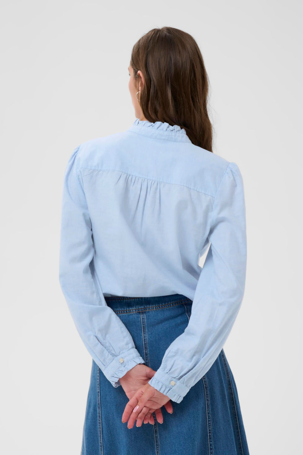 Vue arrière de la Blouse Glessia bleue avec col volanté, manches longues et coupe fluide, portée avec une jupe en denim.