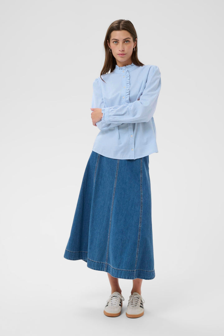 Femme portant la Blouse Glessia avec col volanté et coupe fluide, associée à une jupe en denim, look romantique et élégant.