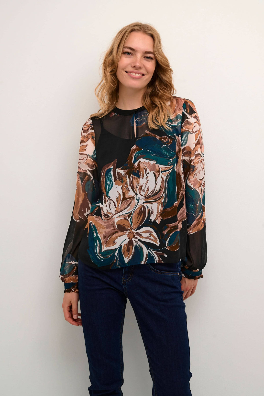 Blouse Jasmina avec imprimé floral, légère transparence et manches longues, portée par un modèle souriant.