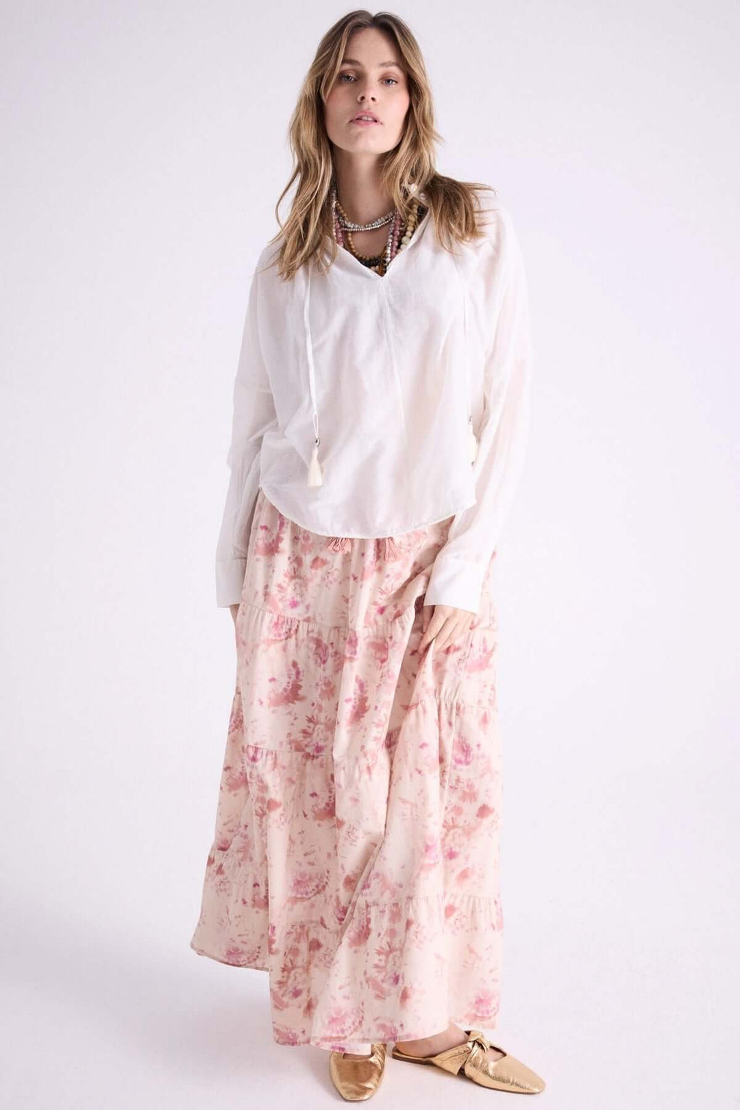 Femme portant une blouse légère à capuche et une jupe longue fleurie, affichant un style bohème et décontracté.