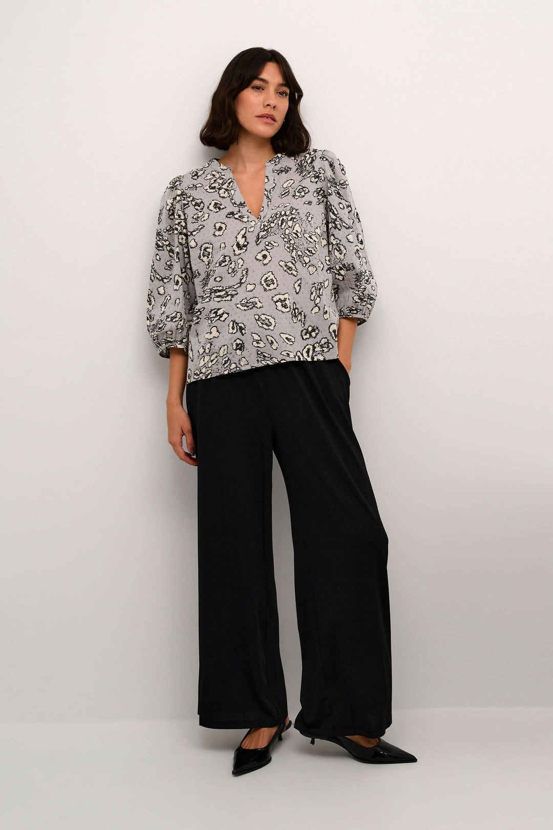 Blouse Liga imprimé léopard avec manches ballons et encolure en V, portée avec pantalon noir.